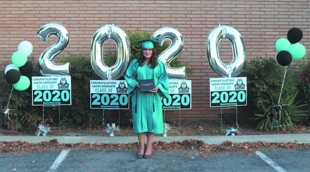 Sharon Lopez, wearing a turquoise graduation gown, cap, and sash, holds her diploma in front of celebratory 2020 balloons. 