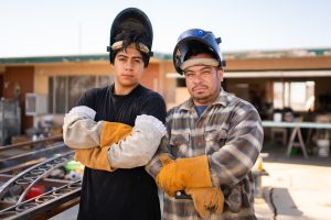 Son Nuri Balderrama and his father Humerto Balderrama stand shoulder to shoulder in protective welding gear, taking career education classes.