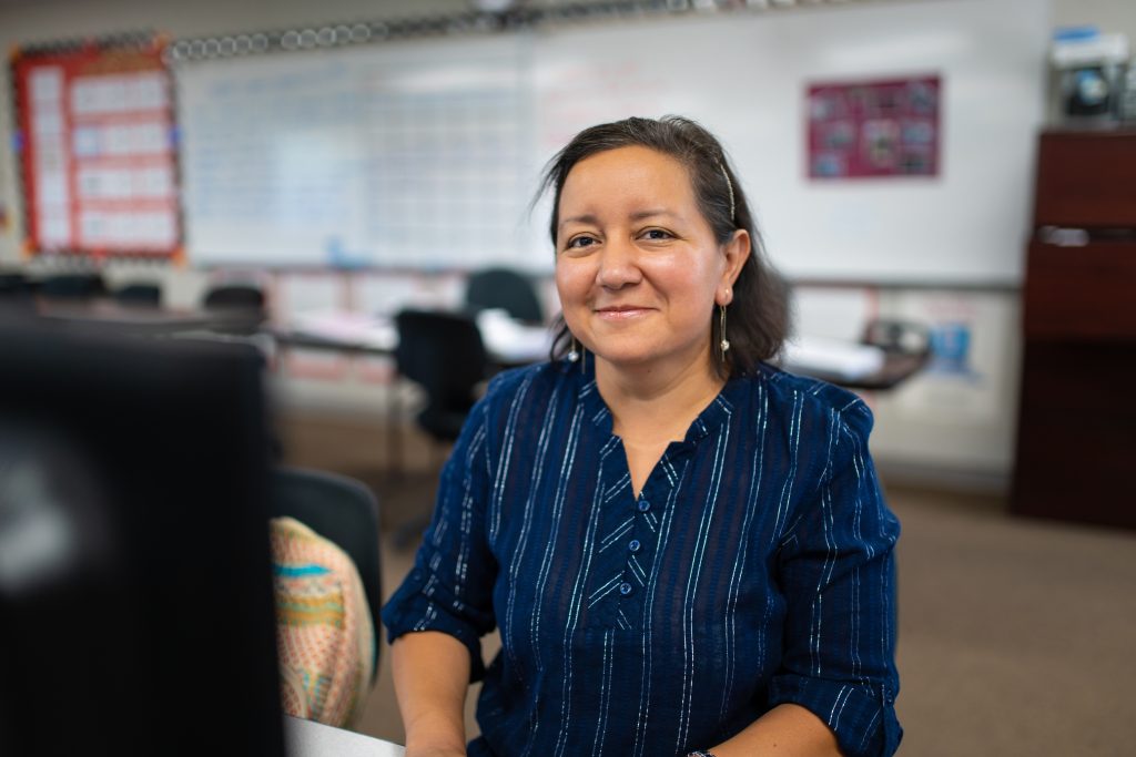 Ruth Yesenia Barrientos-Pineda, a woman in a blue blouse and pearl earrings, smiles for the camera as an Adult Education student who is always looking to improve her future job opportunities.