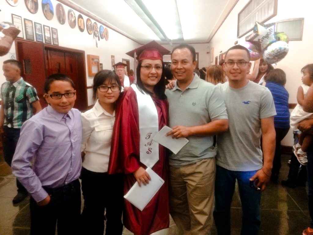 Lesly Pineda in a red graduation gown, posing for the camera with her family after earning her high school diploma from Tulare Adult School.