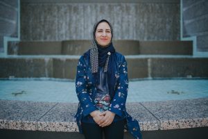 Hamida Hakimi Roshangar, a woman in a hijab and blue patterned blouse, sits on the steps of her adult school campus.