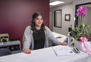 Angel Guzman Lopez (Arenas) stands behind a desk at her office, smiling for the camera.