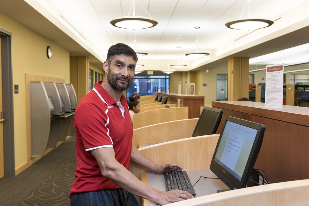 A man is standing at a computer booth inside a library.