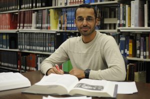 Rafid Alyassiry, an Iraqi man, sits in a library with textbooks open on the desk in front of him.