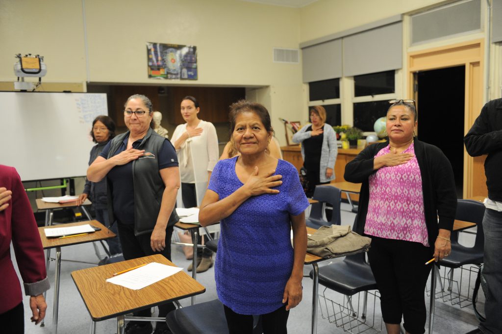 A classroom full of Citizenship adult students practice the Pledge of Allegiance.