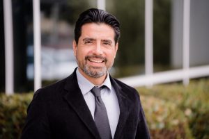 Steve Curiel, a middle aged man with a beard and suit smiles for the camera.