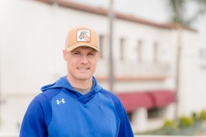 Sergei Koltovoskoi, a man in a blue athletic sweatshirt and a tan baseball cap smiles at the camera.