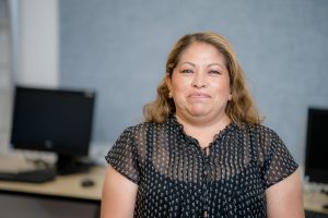 Francisca Juarez, a woman with dark hair with light brown highlights and a polka dot black blouse, smiles for the camera.