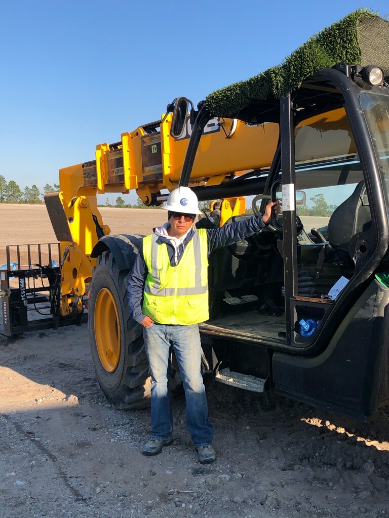 Fernando Zamora in a hard hat and hi-vis vest standing in front of construction machinery