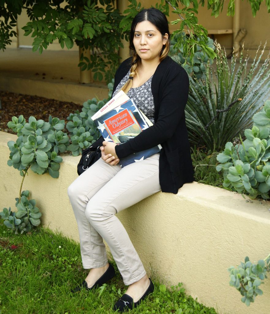 Vivian Gonzalez sits on a low wall outside and holds her school textbooks.