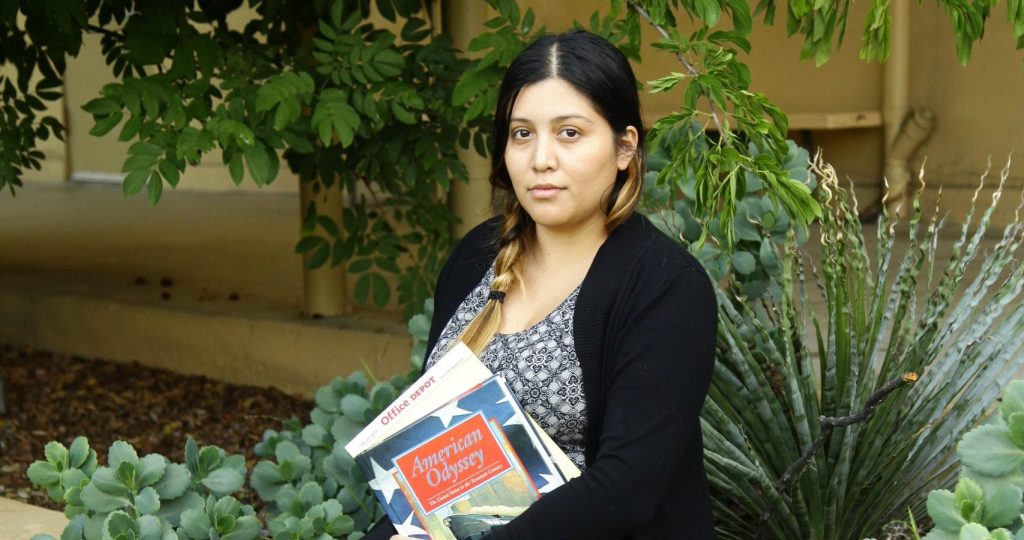 Vivian Gonzalez sits on a low wall outside and holds her school textbooks.