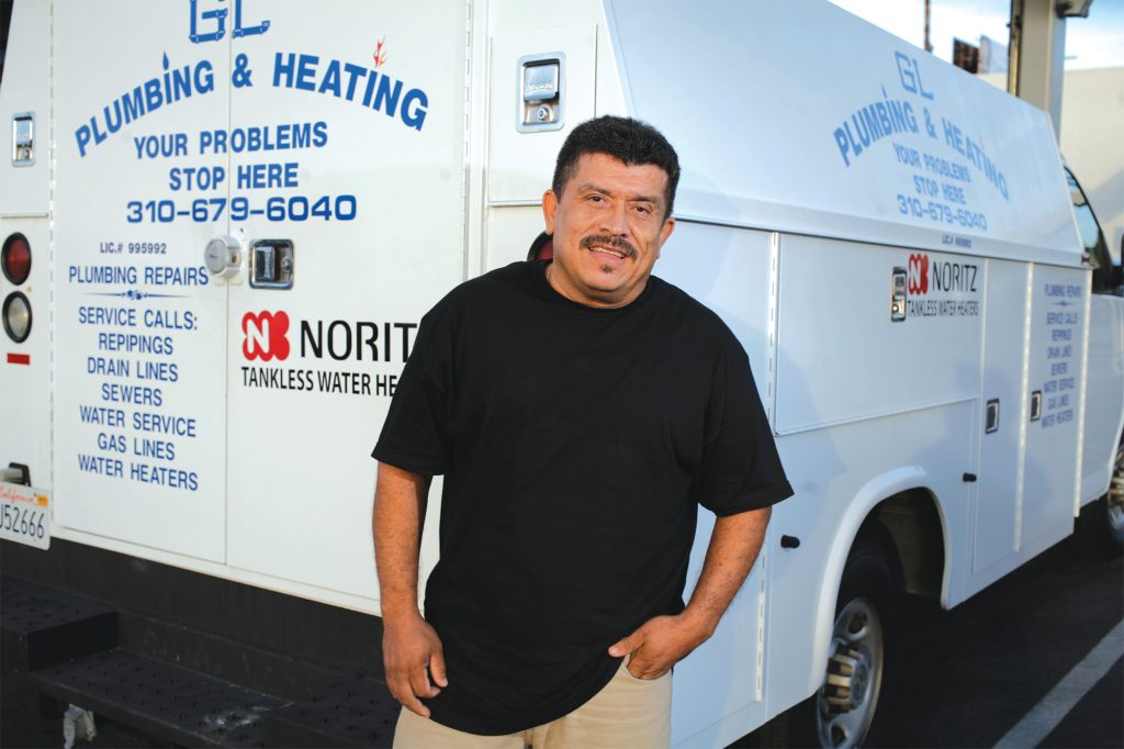 Ramon Gutierrez, a man in a black collared shirt with a mustache, stands on front of one of a work van.