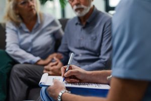 Male doctor writing medical report while visiting senior couple at their home.