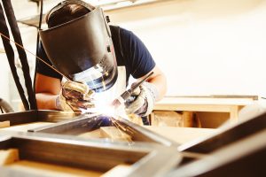 A man in a welder's mask and gloves welding metal