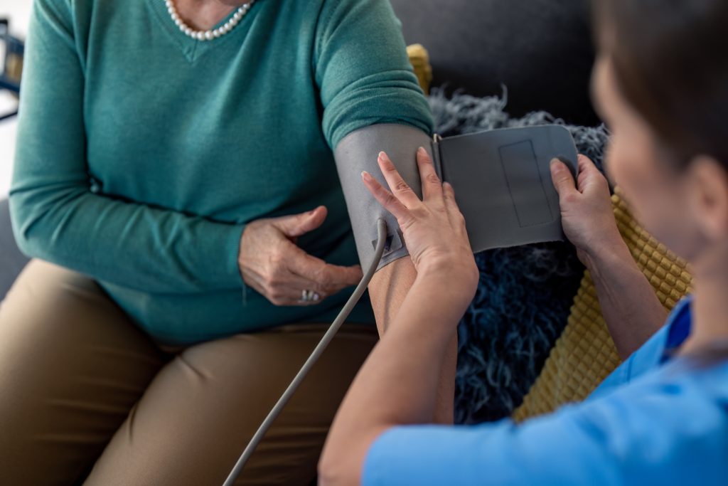 Senior woman visited by home care specialist getting her blood pressure measured. Nurse teaching elderly woman to measure blood pressure at home.