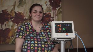 Raven Ortega, wearing colorful scrubs, standing beside medical monitoring equipment.