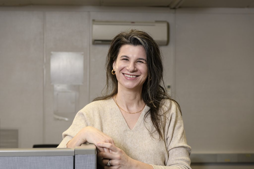 Aline Tet, a woman with brown hair draped over one shoulder and a cream colored sweater, smiles for the camera