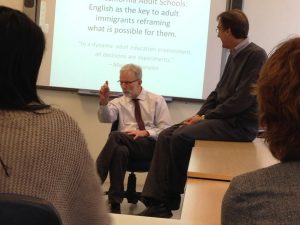 Bob Harper Former executive director of Adult Education, South Bay Consortium for Adult Education, sits in a chair in front of a powerpoint and speaks to a classroom.