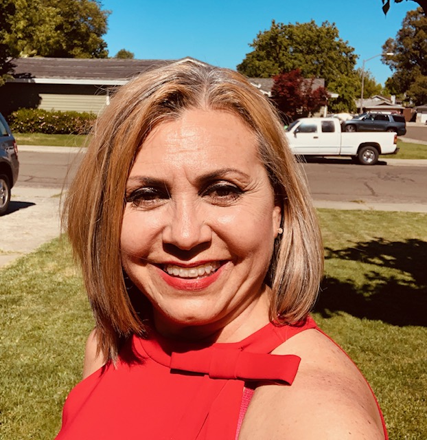 Veronica Flores, a woman with a blond bob and a red sleeveless blouse, smiles in a selfie.