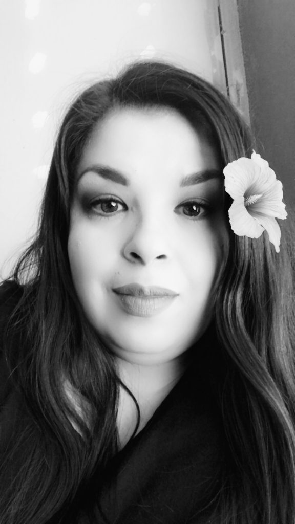 A black and white photo of Maria McLaughlin, a woman with long dark hair and a flower behind her ear.