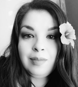 A black and white photo of Maria McLaughlin, a woman with long dark hair and a flower behind her ear.