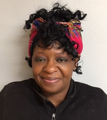 Carlada Thomas, a black woman with her hair gathered into a colorful head scarf, smiles for the camera