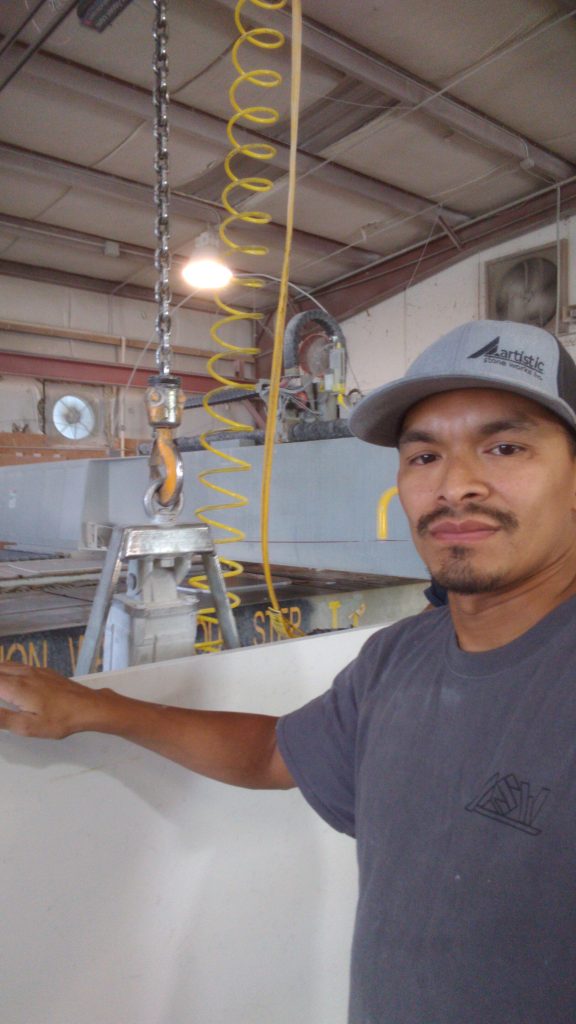 Edgardo Cerna, a man in a baseball cap and gray t-shirt, stands in front of machinery.