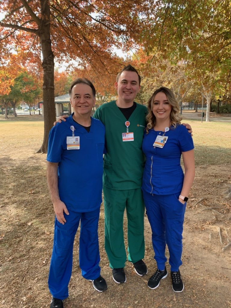 Eddie Egurrola, in blue scrubs (left), stands beside his adult son in green scrubs(center), and his adult daughter in blue scrubs (right)