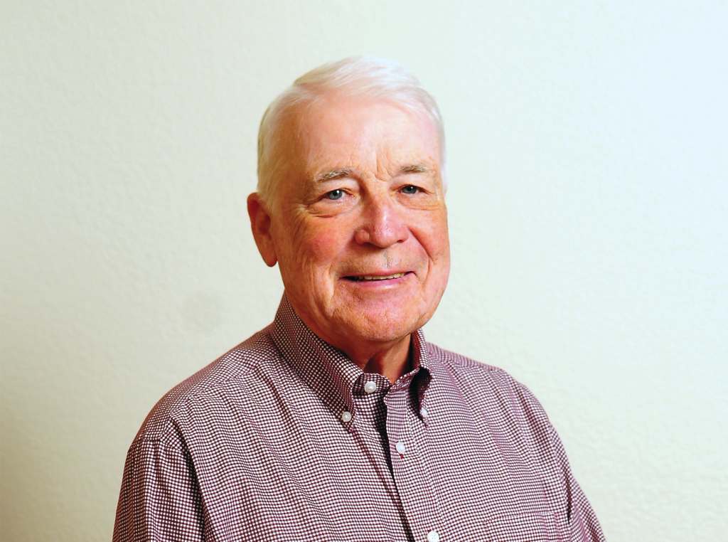 Pat Mead, and elderly mean in a gingham button up shirt, smiles for the camera.