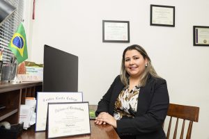 Adriana DeSouza sits in her office with her diplomas and smiles for the camera