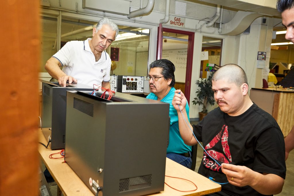 Father-and-son Jose and Felix Cadena work on electrical components in a classroom