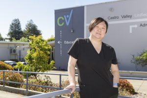 Iris Lim, an Asian woman wearing black scrubs, stands in front of her adult school.