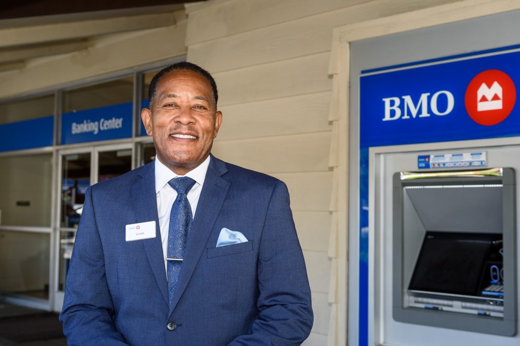 Lee Gardner, a black man in a suit, stands in front of a bank ATM