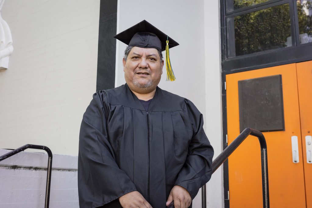 Rodolfo Juarez Ramirez standing on the steps of his campus in his black graduation cap and gown