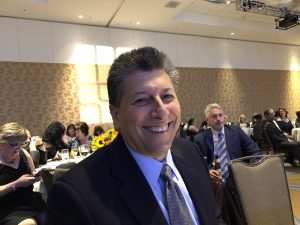 Rocky Bettar, a man with a mid-length gray crew cut in a suit at an event, smiling for the camera