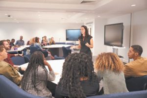 A woman speaking in front of a room full of adult students.