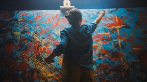 Woman Works on Abstract Painting, in a dark room where the large canvas stands on an easel