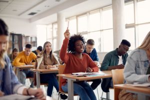 Smiling black woman raising her hand to ask a question during lecture in the classroom.