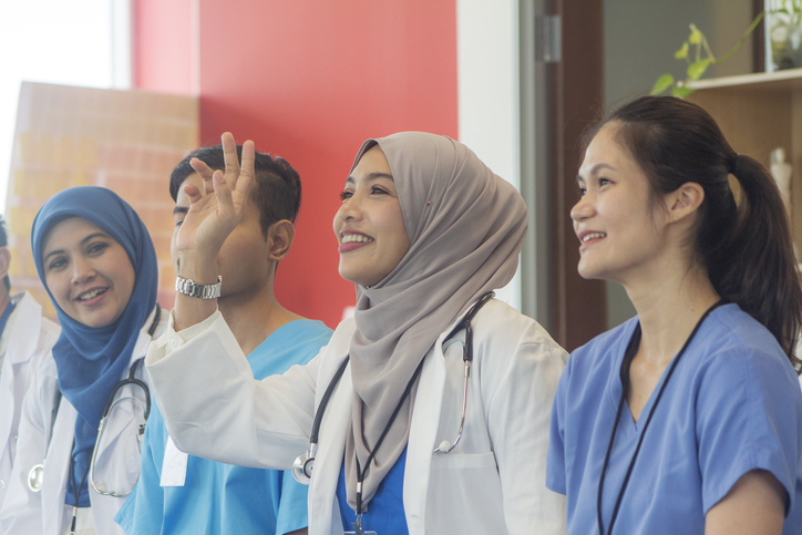 A multicultural group pf health care students, with a woman in a head scarf raising her hand