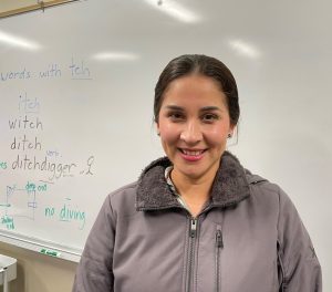 Photo of Ana Ortiz in a gray zip up jacket in front of a whiteboard