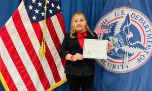 Ermelinda Velasquez holds her citizenship papers and stands in front of United States flags