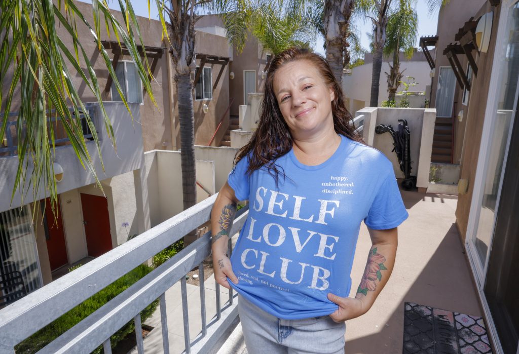 Portrait of Tara Bender displaying her t-shirt with a thoughtful at message at Solutions For Change where she lives.