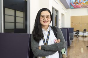 A portrait of Jenny Fang at Berkeley Adult School, wearing a grey sweater and a white collared shirt with a school lanyard