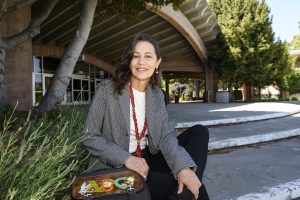 Photo of Clara Ines Barrios in business clothes sitting outside a building near spiky bushes