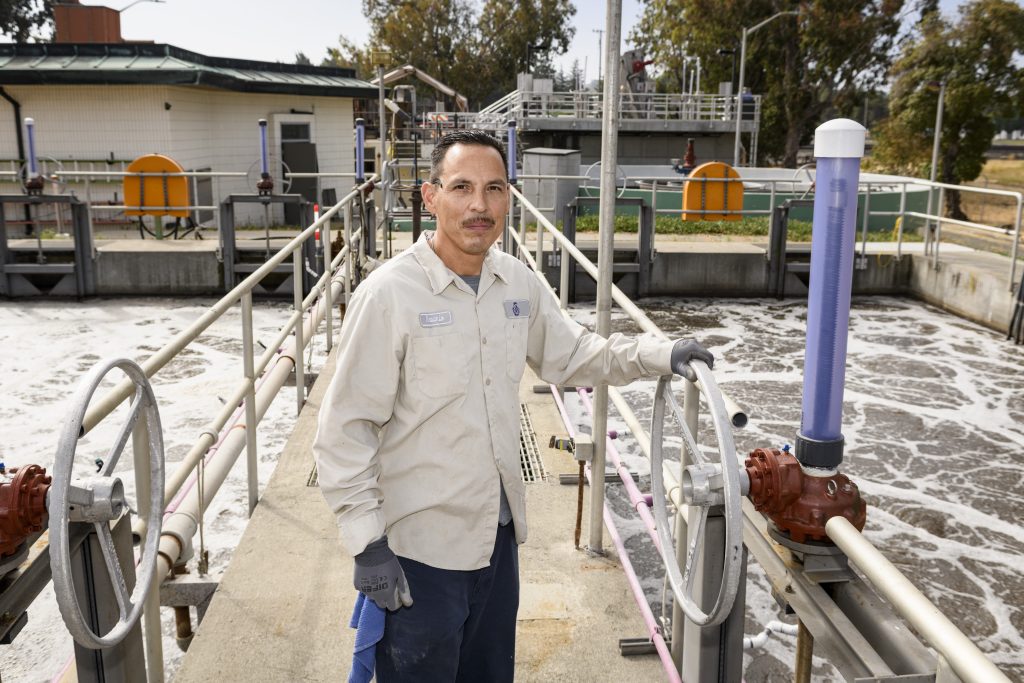 Photo of Nasario Martinez in his work uniform standing in front of the water treatment plant