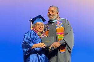 Candice Jarmon in a graduation gown being handed her diploma by Hayward Adult School Director Kwasi Reed.