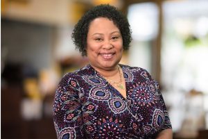 Rhonda Boykin, a black woman in a dark purple paisley print, smiles for the camera