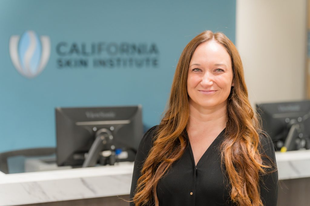 Vanessa Stokes standing in front of a desk and computer at the California Skin Institute and smiling for the camera