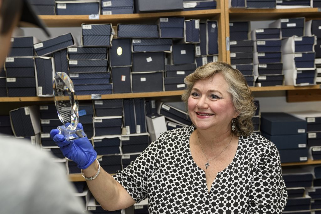 Laura Martinez, a woman in a black and white patterned blouse and wearing blue latex gloves, shows something in a plastic wrapper to another person