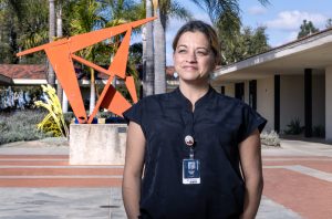 Portrait of student Tiffany Reid at MiraCosta College after her morning English class. She wearing her medical scrubs. In the distance is the school’s sculpture at the 3500 Building courtyard. Photo by Charlie Neuman